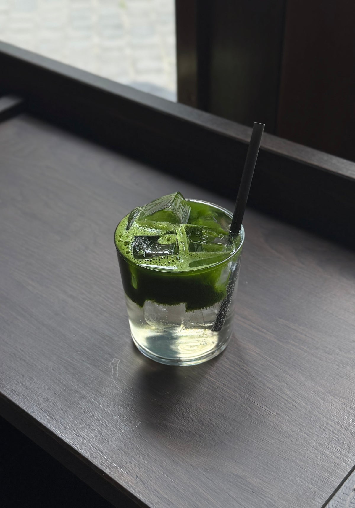 A glass of matcha lemonade with layered green matcha and sparkling water over ice.